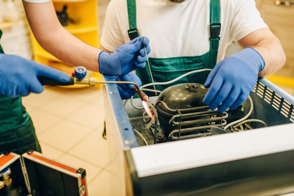 Workers with burner repairs refrigerator at home